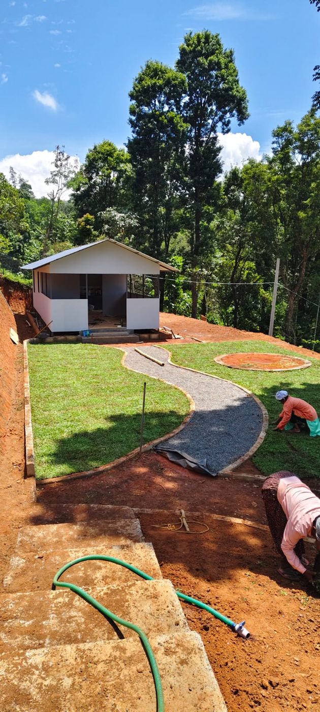 A white cabin with a covered verandah above a new lawn and a curving gravel path