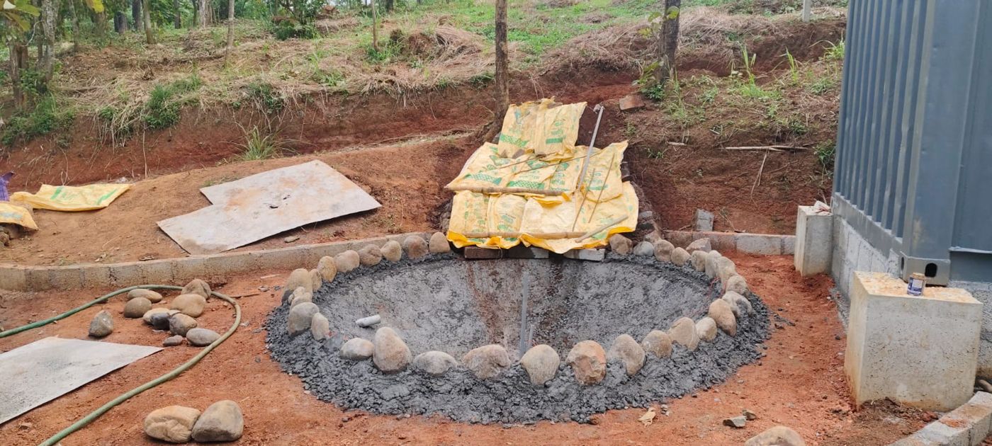 A round koi pond ringed with river stones being built beside a cabin